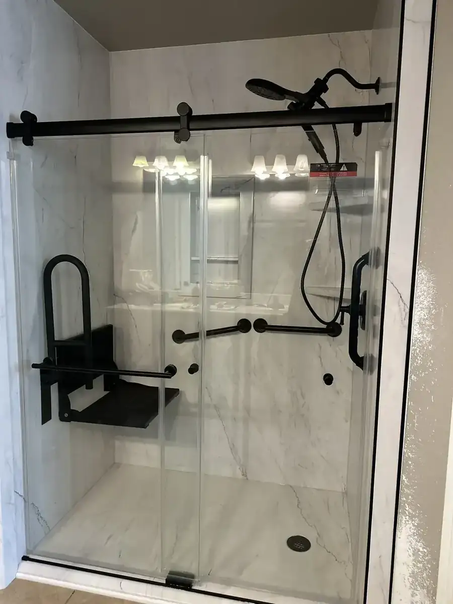 Marble-look walk-in shower with a black slider, a fold-down seat and several matte black grab bars