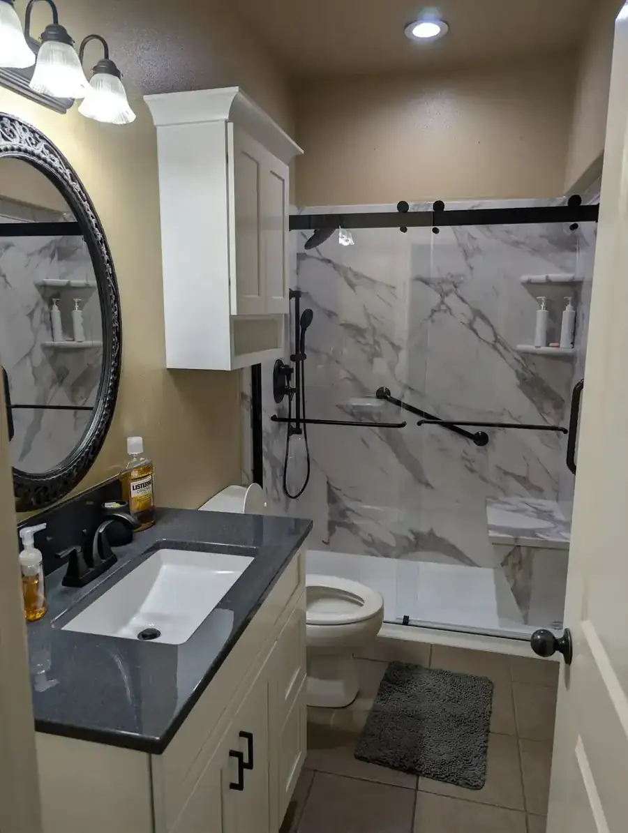 A finished small bathroom with a marble-look walk-in shower, black slider door and a vanity