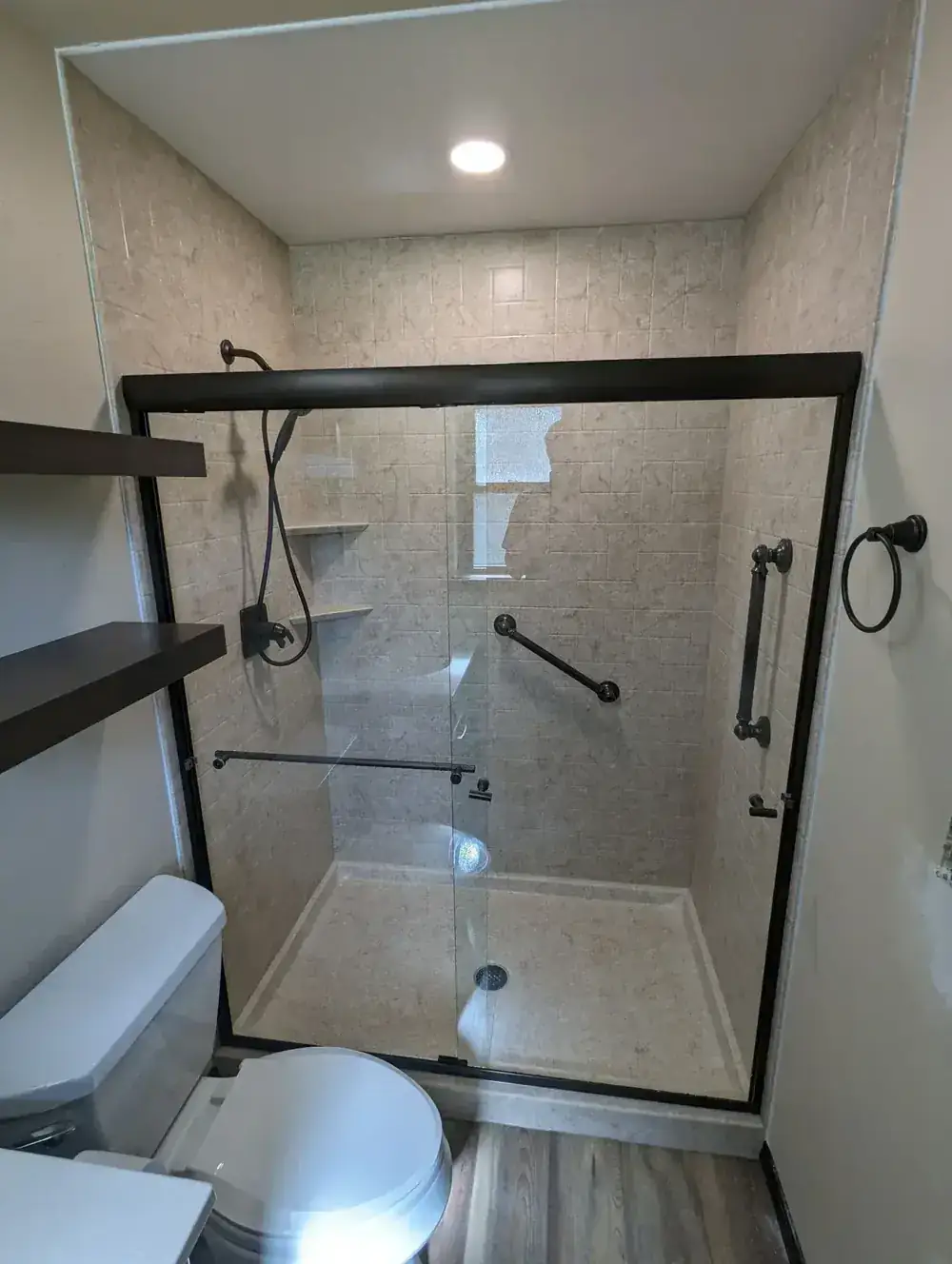 A Bella Vista walk-in shower with a black slider, stone-look panels, grab bars and floating shelves