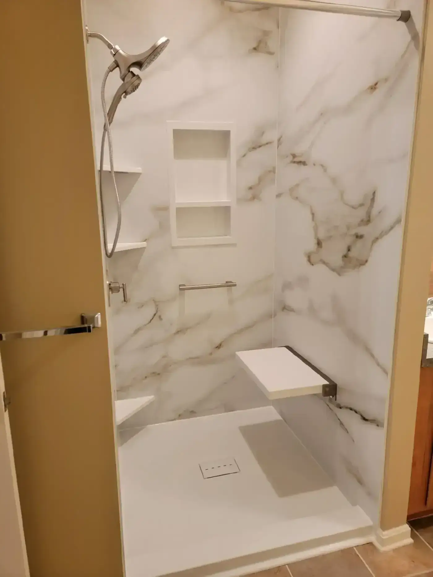 A Bentonville shower with Calacatta-gold panels, a recessed niche and a fold-down seat