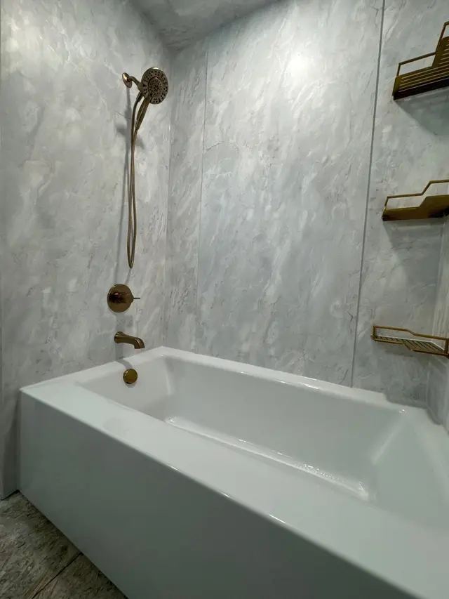 Grey marble-look surround over a soaking tub with bronze fixtures and shelves