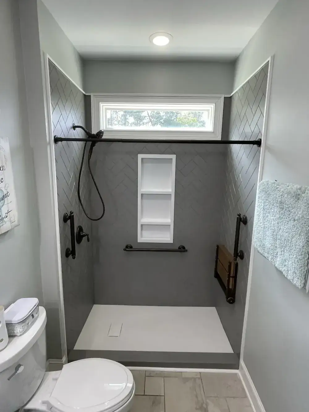 Cave Springs walk-in shower with matte black grab bars, a fold-down teak seat and a transom window