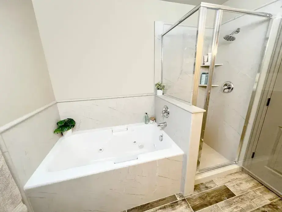 Corner soaking tub beside a glass walk-in shower with white panels