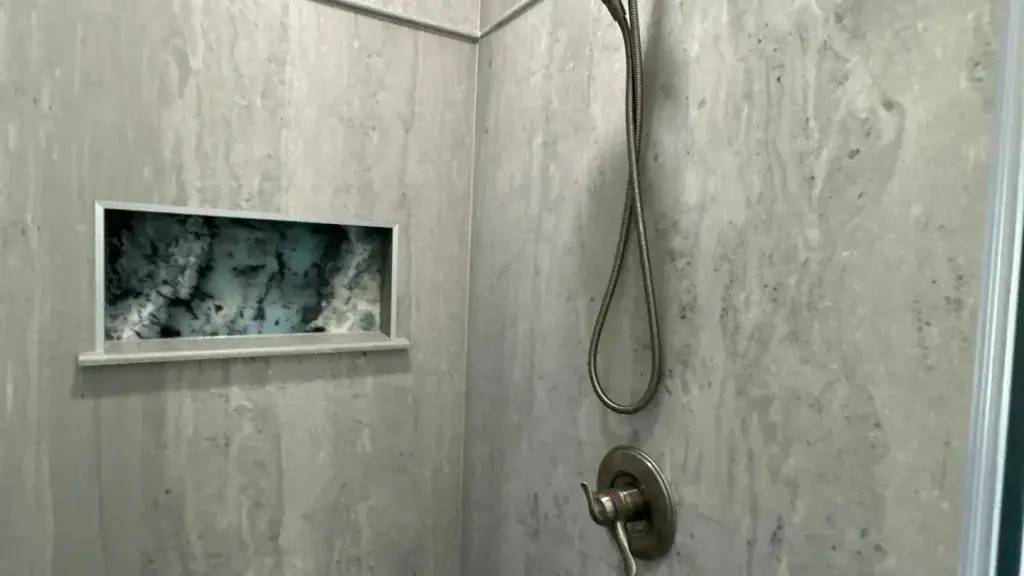 Close-up of a grey stone-look shower panel wall with a recessed niche and a wand