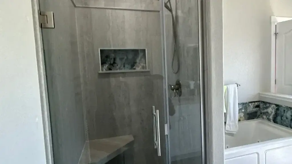A grey stone-look walk-in shower with a blue stone niche beside a white jetted tub