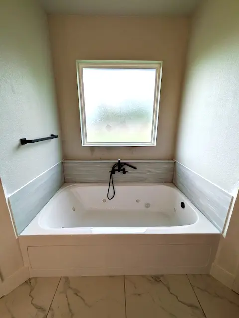 Jetted tub installed under a window with a marble-look floor