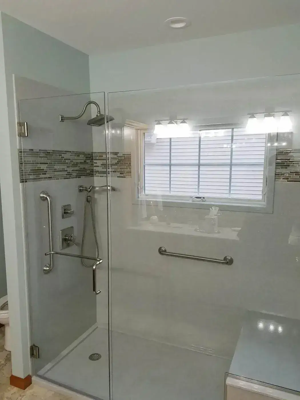 Walk-in shower beneath a window with a mosaic band, a bench and several grab bars